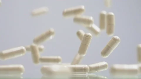 White elongated supplement capsules falling in slow motion Video stock 169223327