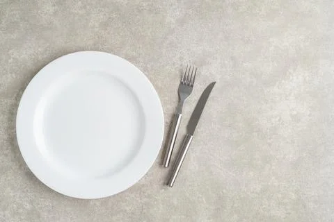 White empty ceramic plate with fork and knife over stone background with co.. Stock Photos