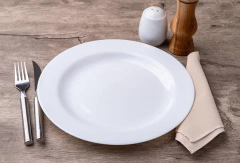 White empty ceramic plate with fork and knife, pepper grinder, salt and nap.. Stock Photos