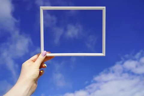White empty horizontal frame in female hand against blue sky. Space for your Stock Photos