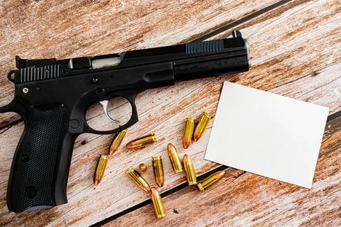 White empty note next to bullets and black gun on wooden plank background Stock Photos