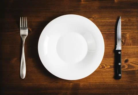 White empty plate with a fork and knife on a wooden table. Foto stock