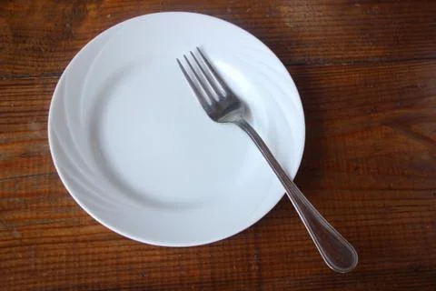 White empty plate with fork on a old wooden board on a dark wooden background Stock Photos