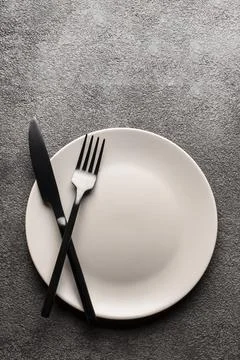 A white empty plate on a gray background and a fork and knife. Concept for a Foto stock