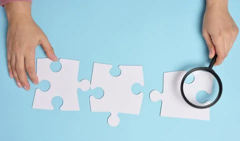 White empty puzzles and a magnifying glass in hand on a blue background, to.. 스톡 사진