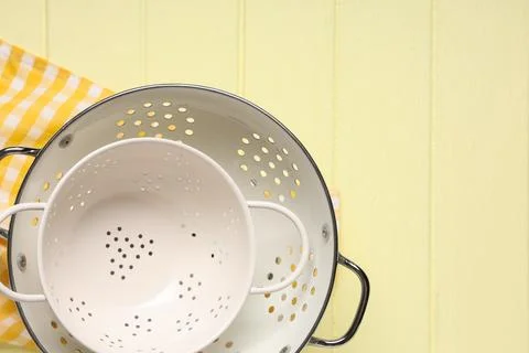 White enamel colanders stacked on a yellow gingham towel and light yellow woo Stock Photos