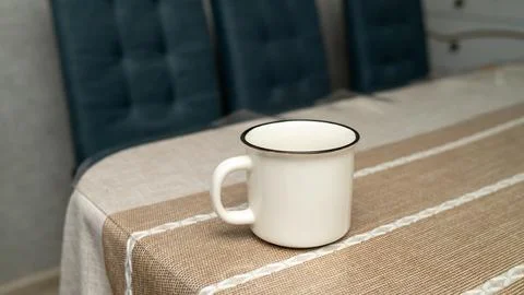 White enamel mug on patterned tablecloth in cozy kitchen setting Stock Photos