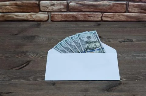 White envelope with five hundred dollars on a wooden table near a brick wall. Stock Photos