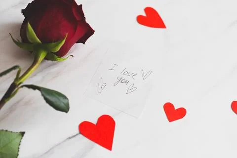 A white envelope lies on a table, adorned with heart-shaped confetti and a re Stock Photos