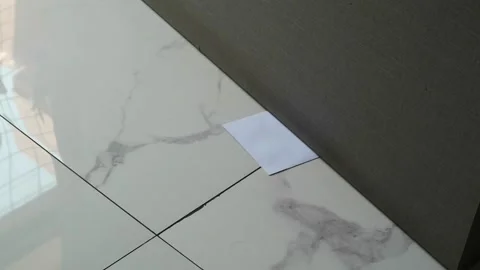 A white envelope with a message slipped under a door on a marble floor Stock Footage 330480732