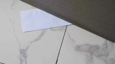 A white envelope with a message slipped under a door on a marble floor Stock Footage 330480758