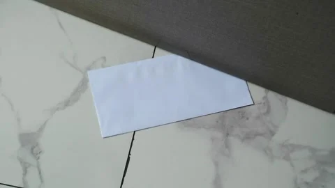 A white envelope with a message slipped under a door on a marble floor Stock Footage 330480759