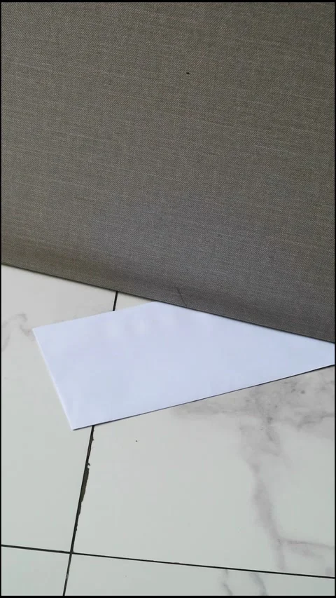 A white envelope with a message slipped under a door on a marble floor Stock Footage 330480767