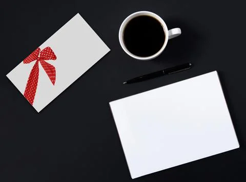 White envelope with a painted red bow is on the table next to a cup of coffee Stock Photos