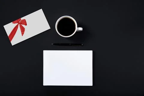 White envelope with a painted red bow is on the table next to a cup of coffee Stock Photos