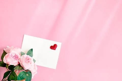 White envelope with red silk heart and bouquet of rose on light pink backgr.. Stock Photos