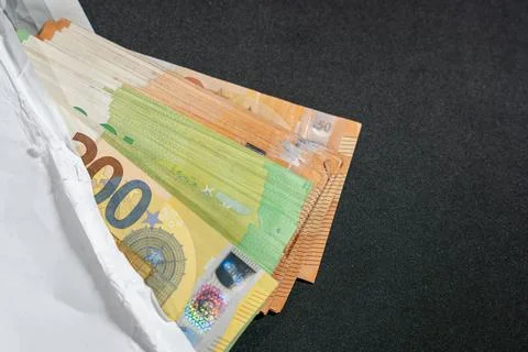 A white envelope reveals a stack of euro banknotes on a dark background. 스톡 사진