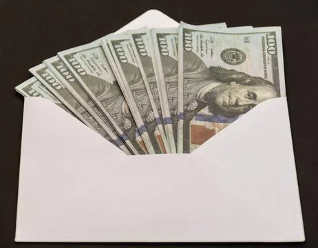 White envelope with several hundred dollar bills inside placed on dark backgr Foto stock