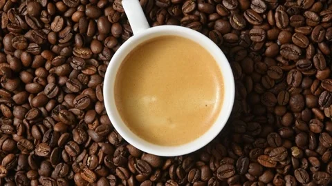 White espresso cup rotates on roasted coffee beans in top view for cafe and Stock Footage 345222581