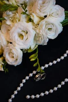 White eustoma flowers and roses, a pearl necklace and wedding rings create a  Stock Photos