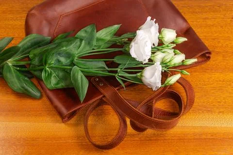 White eustoma lying on brown leather women's bag, top view Stock Photos