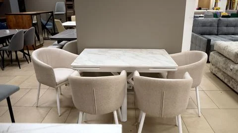 White extending dining table with beige upholstered chairs in furniture store Stock Photos