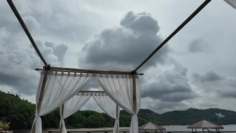 White fabric canopy frames an overcast tropical landscape with hills and water. Video stock 343397133