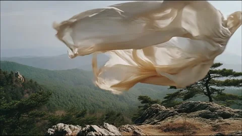 White fabric flows gracefully against a backdrop of mountains and sky Video stock 314717949