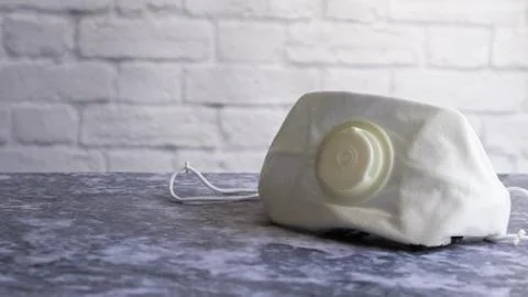 White face shield with flap on a gray table against a white brick wall with c Stock Photos