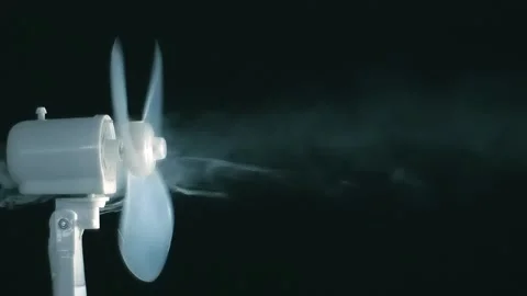 A white fan on a black background rotates and blows a stream of smoke Stock Footage 313182387