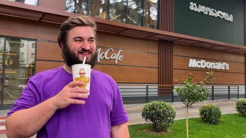 White fat man with beard, purple t-shirt, stands near fast food restaurant Video stock 338312824