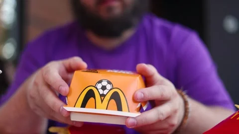White fat man with beard twists and turns yellow paper box with Big Mac burger Video stock 341275346