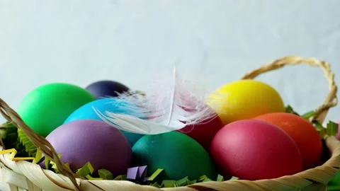 White feather falls on a basket of colored Easter eggs side view closeup Stock Footage 235811165