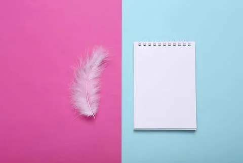 White feather next to a blank notepad on pink and blue background Stock Photos