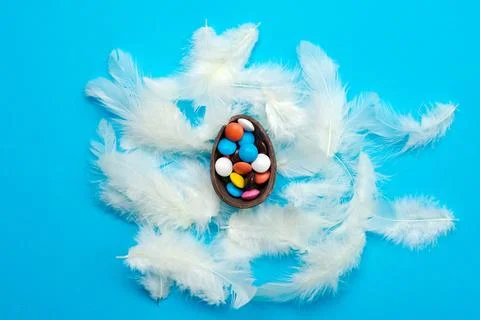White feathers lie on the blue Easter background. Multi-colored candies in .. Stock Photos