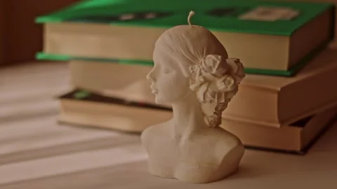 White female bust candle on stack of vintage books Stock Footage 339774414