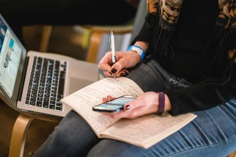 White female taking notes on her notebook with her smartphone Stock Photos