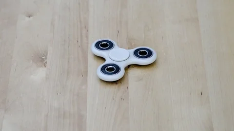 A white fidget spinner stress relieving toy spinning on wooden background Stock Footage 80399798