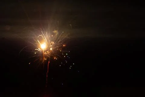 A white firework explodes in the center of the night sky, sending soft streaks. Stock Photos