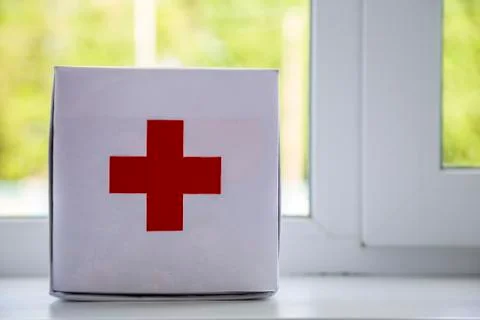 White first aid kit with red cross indoors on windowsill on blurred backgroun Stock Photos