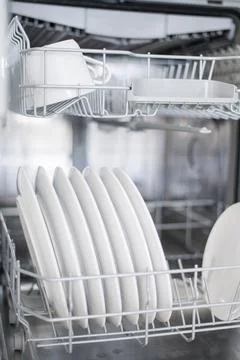 White flat plates are loaded into the dishwasher Stock Photos