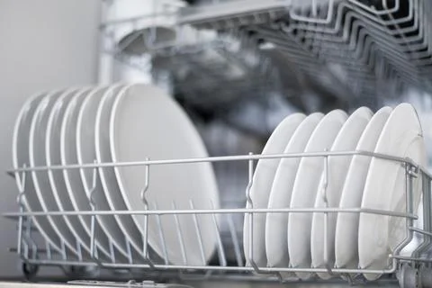 White flat plates are loaded into the dishwasher Stock Photos