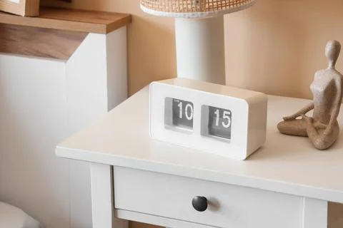 White flip clock displaying 10:15 AM on a modern nightstand with decorative e Stock Photos