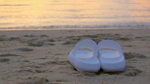 White flip flops lying on the sand of the beach, vacation concept. Slippers in Video stock 220082438