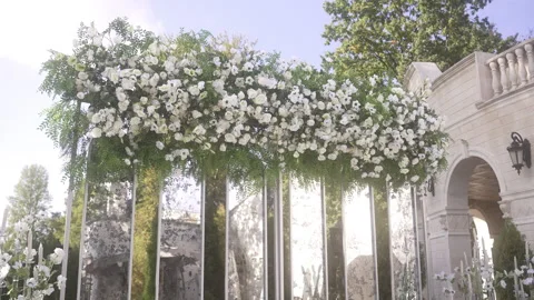 White flowers cascade from a tree in front of a building under a cloudy sky Vidéo 265575483