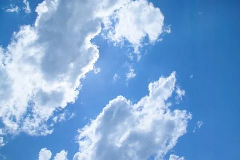White fluffy clouds in a bright blue sky on a sunny day. Stock Photos