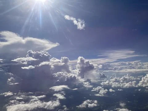 White fluffy clouds filled the sky and radial beams spread from the bright sun Foto stock