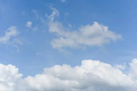 White fluffy clouds float gently in a clear blue sky on a bright sunny day... Stock Photos