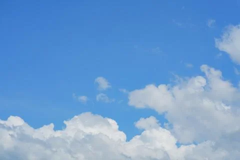 White fluffy clouds float gently in a clear blue sky on a bright sunny day... Stock Photos