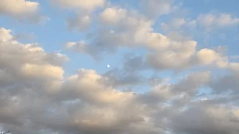 White fluffy clouds illuminated by soft sunlight and small moon in bright b.. Stock Photos